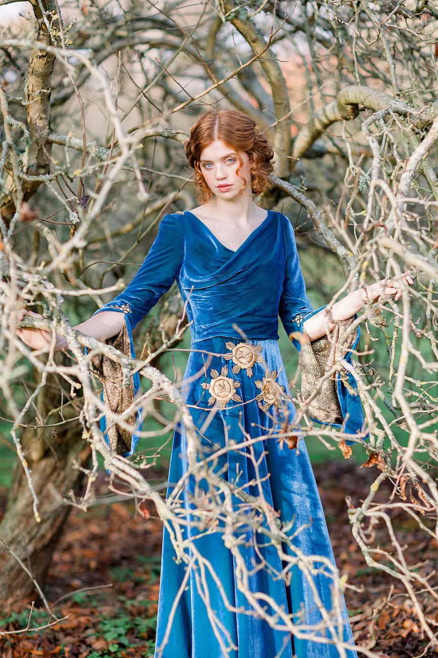 Baroque Wedding with bride standing in deep blue velvet dress behind branches of a tree