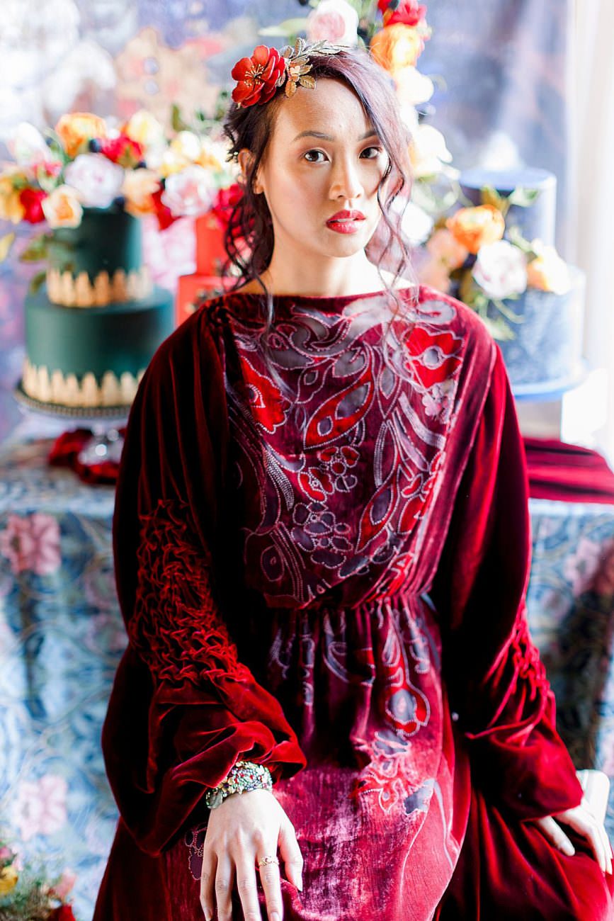Baroque wedding inspiration with a bride in a red velvet dress sitting in front of cakes