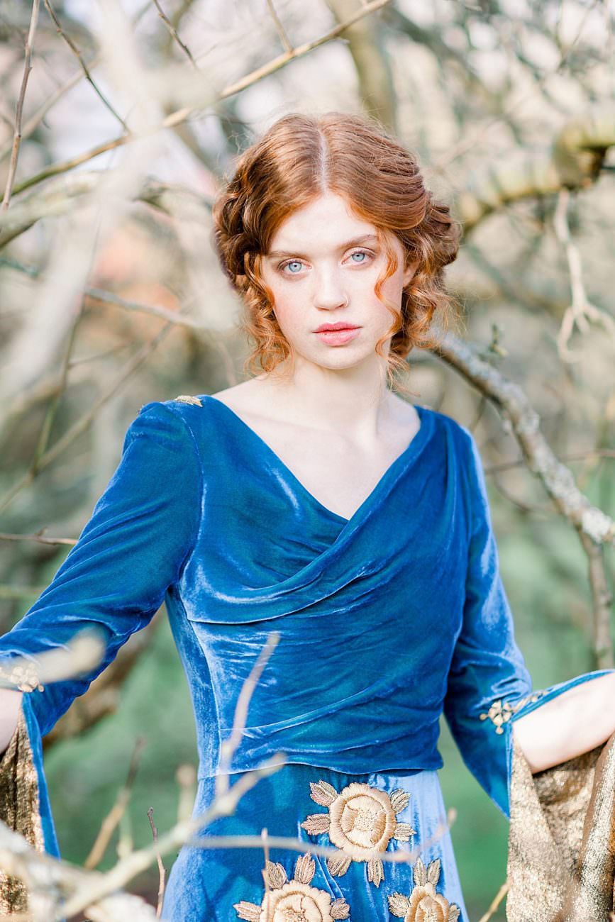 Baroque wedding inspiration with a model in a blue velvet dress standing behind branches