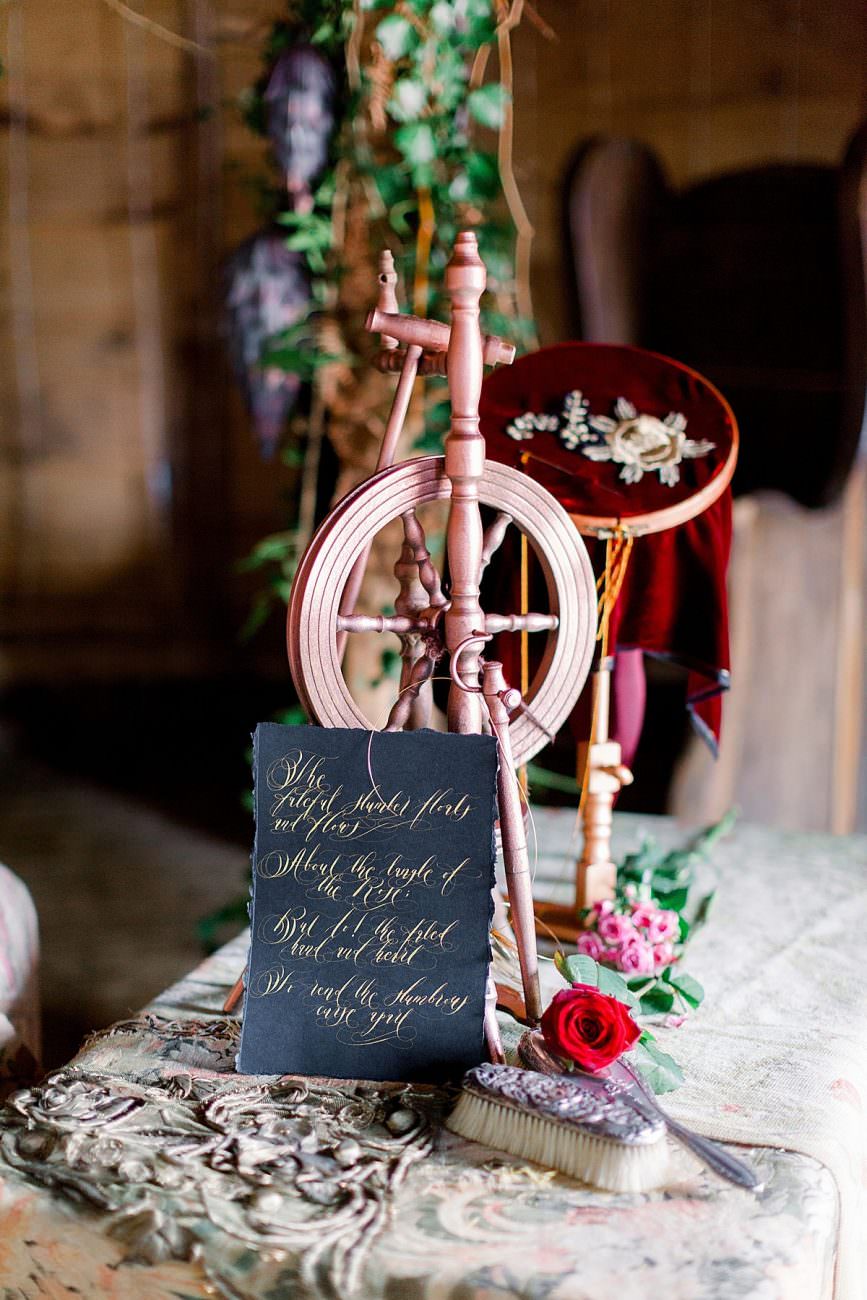 gold calligraphy poem on black paper next to a wooden spinning wheel