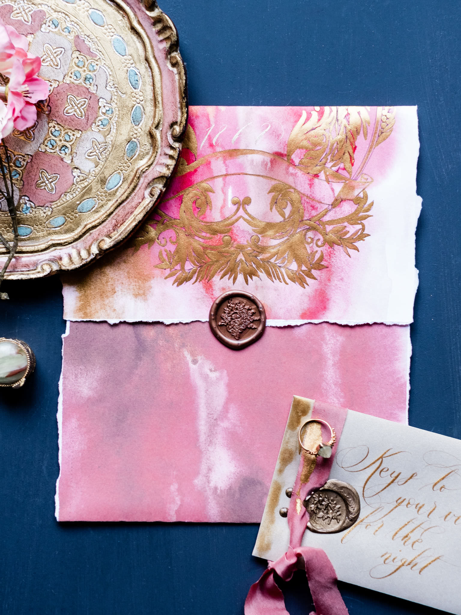 Handmade envelope in bright pink watercolour wedding stationery with crest design hand painted in gold ink